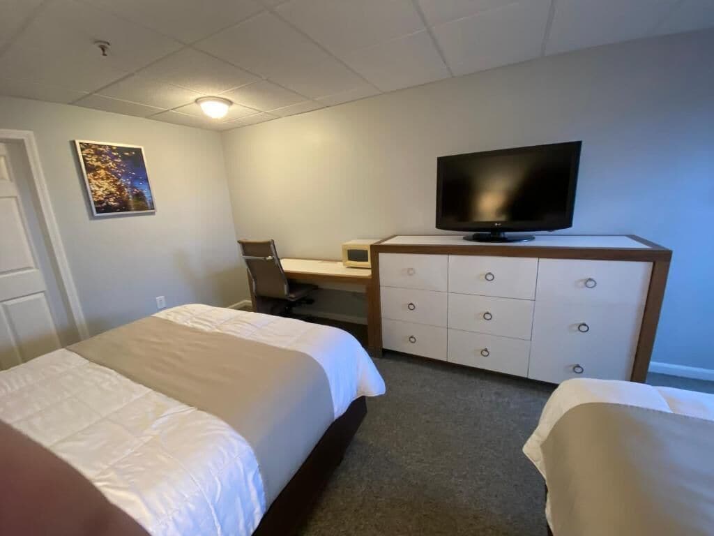 A hotel room with two beds, a desk, a television, and a dresser.