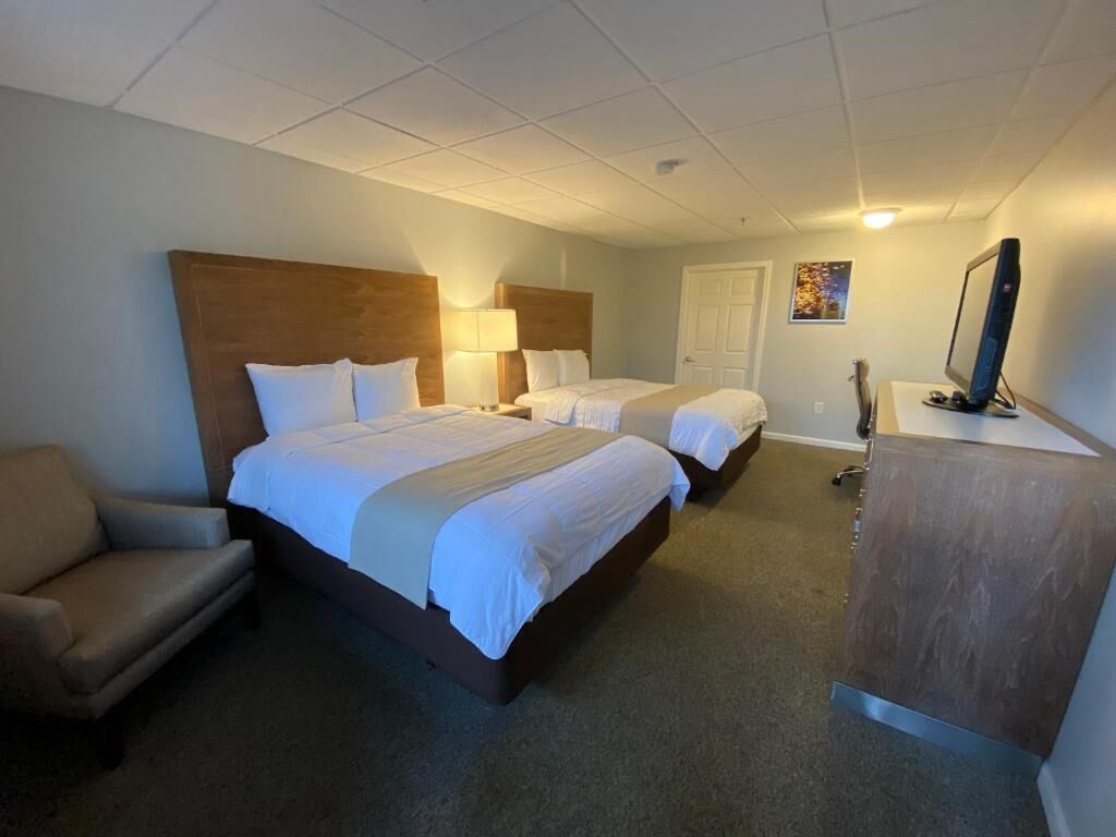 A hotel room with two beds, a desk, a chair, and a television.