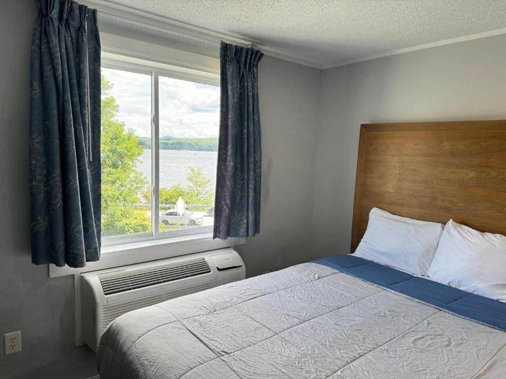Ein Hotelzimmer mit einem großen Bett, einem Holzkopfende, einem Fenster mit Vorhängen und Blick ins Freie.