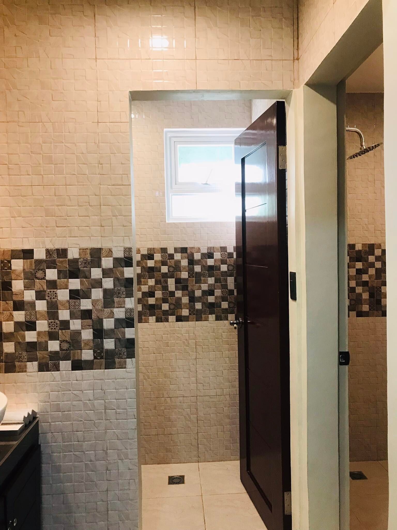 A bathroom with a tiled wall, a shower area, and a door.