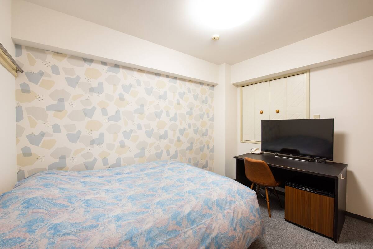A bedroom with a bed, a desk with a television, and a wardrobe.