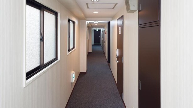 A hotel corridor with a carpeted floor, wooden doors, and a window on the left. - Yokohama Sakuragicho Town Hotel 24 (Yokohama)