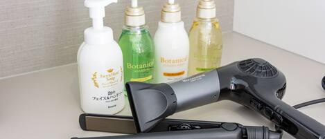 A hairdryer, a brush, and four bottles of hair care products on a countertop.