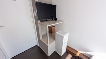 Una habitación compacta con televisión integrada, un pequeño electrodoméstico blanco y un estante de madera.