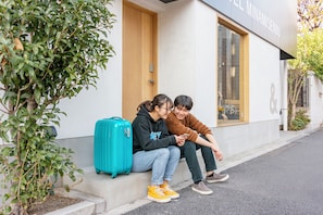 Dos personas sentadas en los escalones frente a un edificio con puerta de madera y ventana.