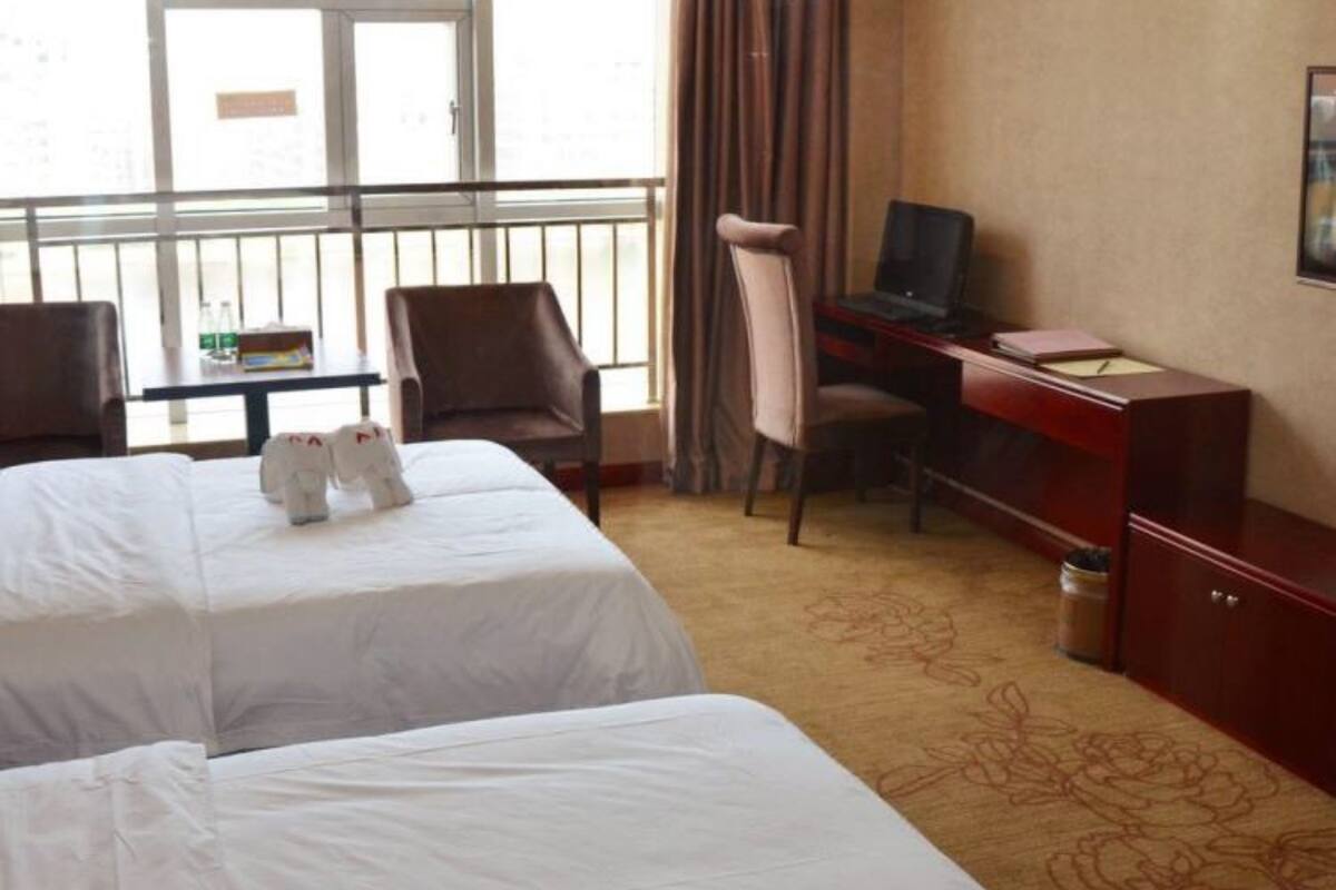 Ein Hotelzimmer mit zwei Betten, einem Schreibtisch mit einem Laptop, einem Stuhl und Blick durch große Fenster nach draußen.
