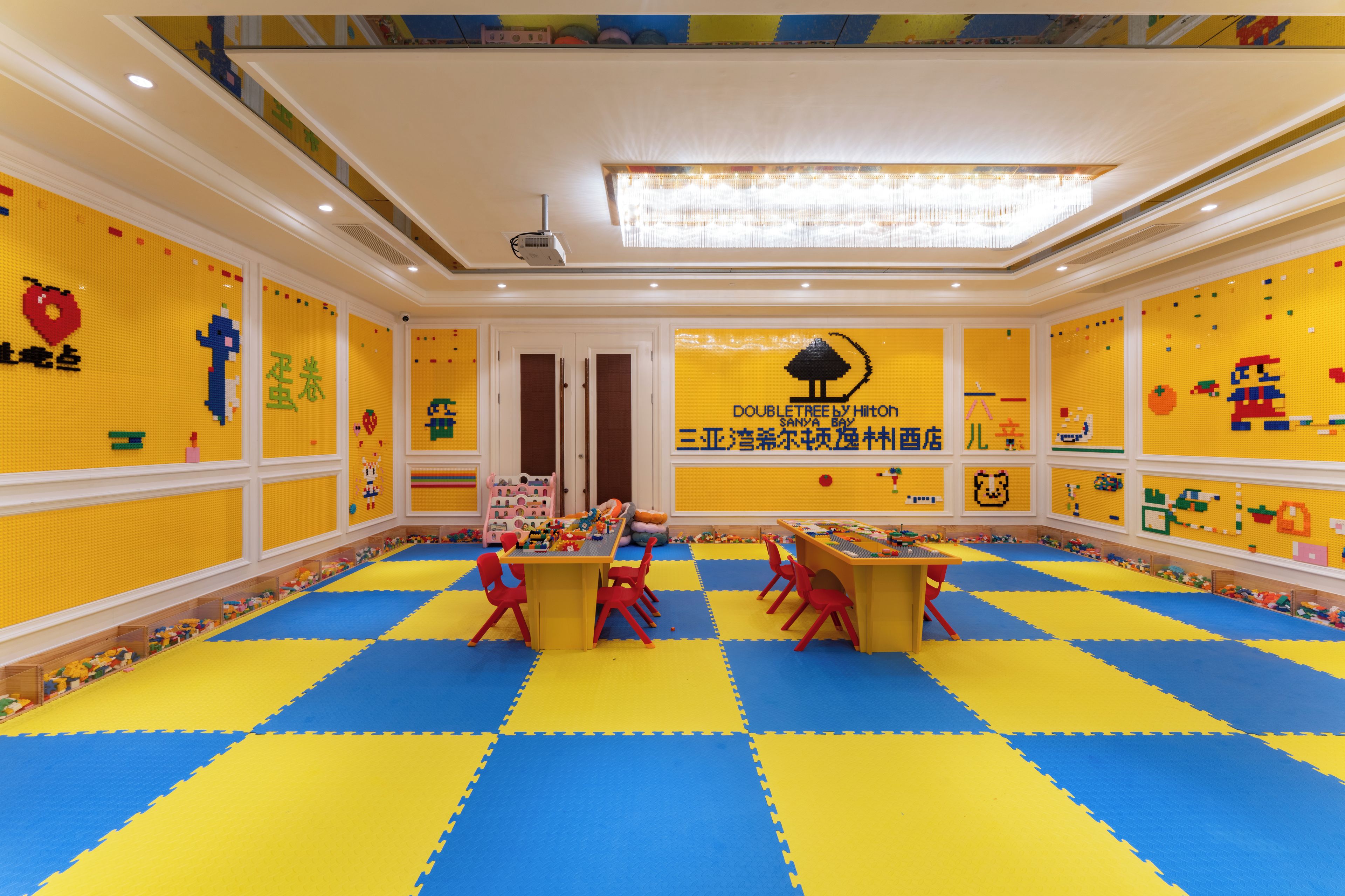 A children's playroom with a blue and yellow floor, a table with chairs, and walls decorated with colorful patterns.