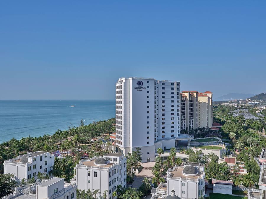 A high-rise hotel with a view of the sea, surrounded by palm trees and other buildings.