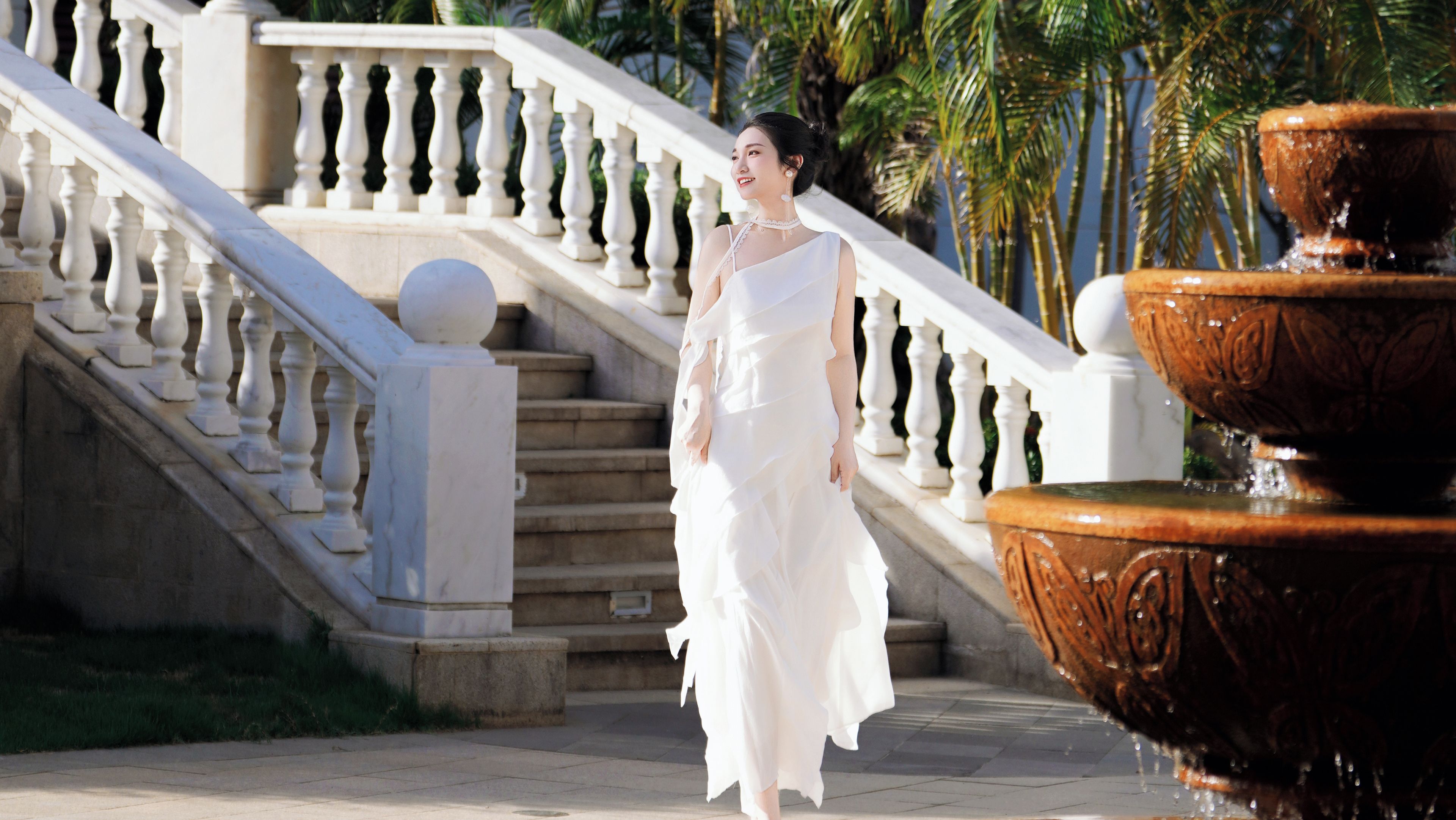 A person in a white dress walking on a stone staircase with a fountain.