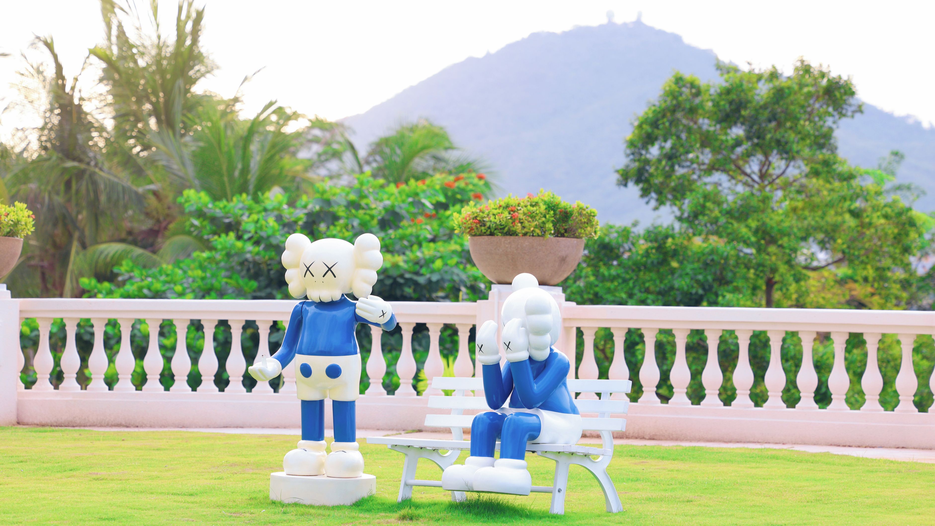 Two statues on a white bench with a balustrade in the background.