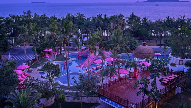 A resort with a pool area, palm trees, and a view of the sea.