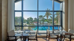 A dining area with a large window overlooking a pool and tropical landscape.