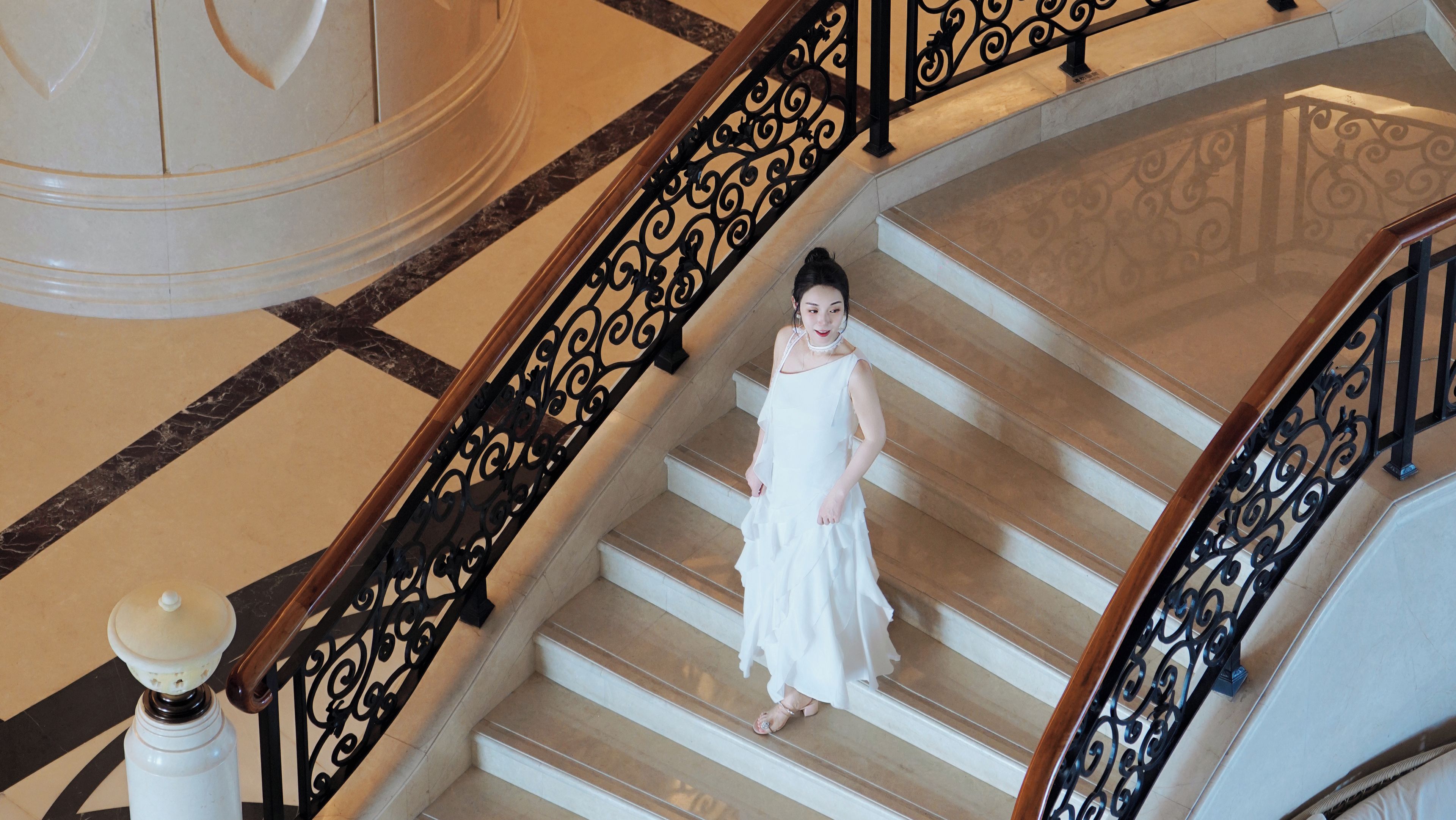A person descending a grand staircase with ornate black balustrades and marble steps.