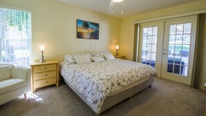 A bedroom with a bed, two bedside tables, a nightstand, a ceiling fan, and a large window with curtains. - Four Bedroom Comfort  4668 Home by RedAwning (Hernando)