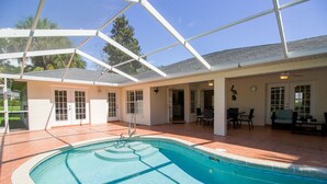 A covered swimming pool area with a patio, chairs, and a door leading to an interior space. - Four Bedroom Comfort  4668 Home by RedAwning (Hernando)