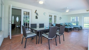An open-plan living area with a dining table, chairs, and a sofa. There are ceiling fans, a clock, and a door leading to another room. - Four Bedroom Comfort  4668 Home by RedAwning (Hernando)
