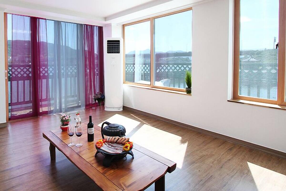 A spacious room with a wooden floor, a large window with a view, and a sliding door with a view.