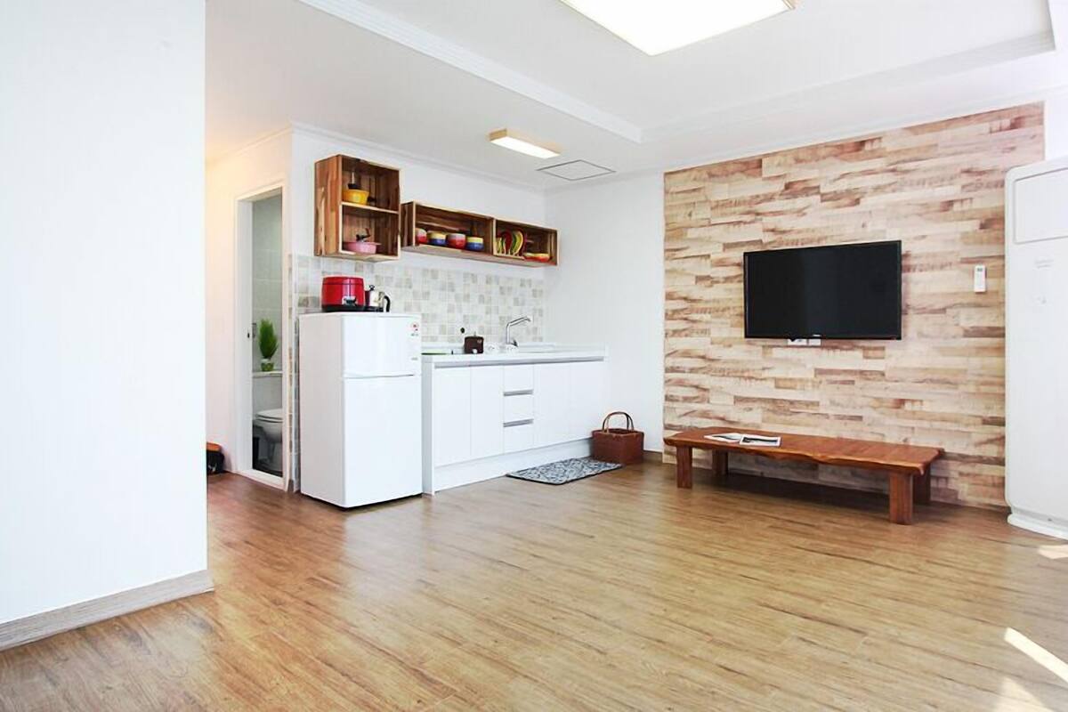 A modern kitchen with white cabinetry, a built-in oven, and a wooden wall with a flat-screen TV.