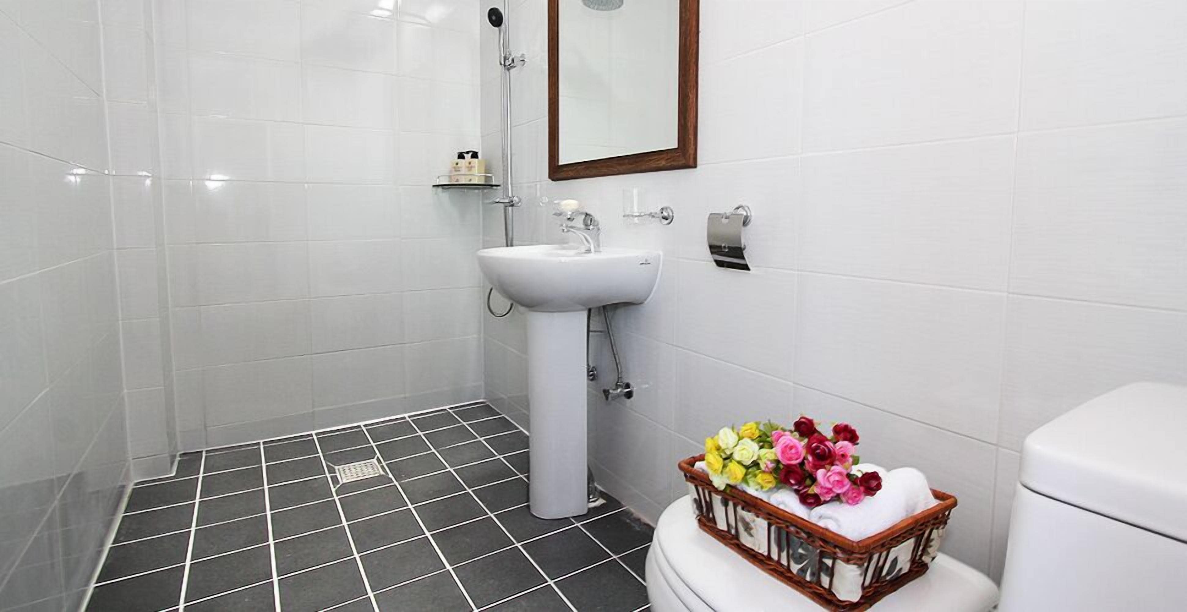 Een badkamer met een wit wastafel, toilet en douche. Op het toilet staat een mand met bloemen.