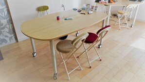 A room with a wooden table, two chairs, a desk with a computer, and various items on the table. - Guest House Ioly Osaka - Hostel (Fujiidera)