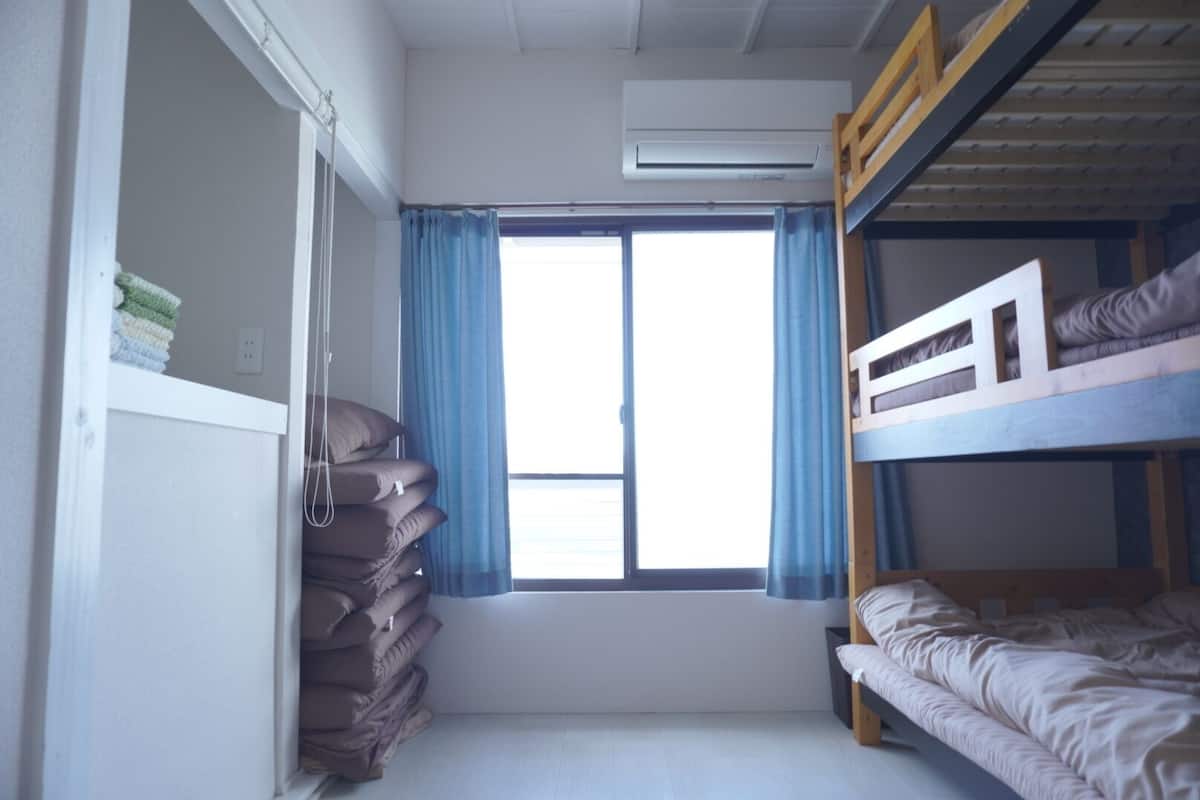 Une chambre avec un lit superposé, une fenêtre, des rideaux et une pile de couvertures pliées.