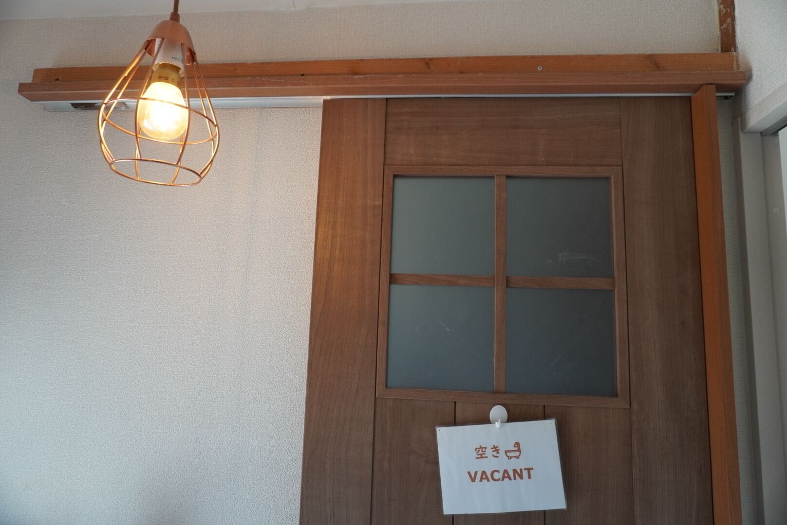 A wooden door with a 'VACANT' sign, a light fixture above it, and a wooden beam above the door.