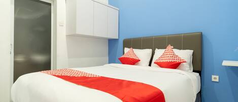 Un lit bien fait, recouvert d’une couvre-lit blanche et rouge, avec deux oreillers aux motifs rouges et blancs, et une tête de lit grise.
