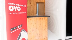 A reception desk with a wooden panel design, a glass door, and a red promotional stand for OYO Hotels.