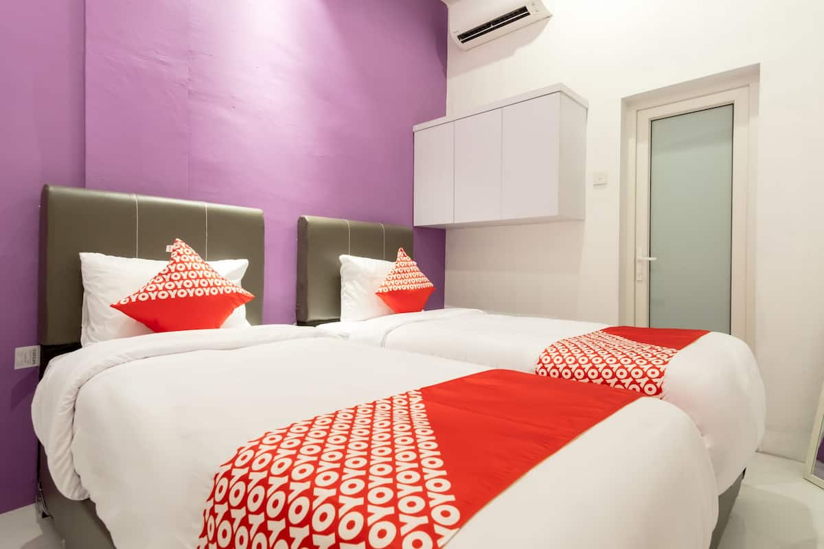 A hotel room with two beds, purple walls, white and red bedding, a white wardrobe, and an air conditioning unit.