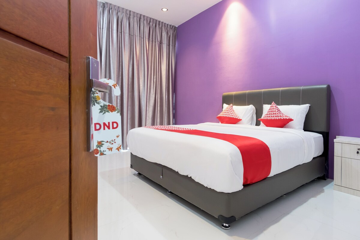 A modern hotel room with a large bed, purple walls, and a wooden wardrobe.