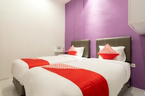 Een tweepersoonsbed met rode en witte beddengoed, een nachtkastje met een fles erop, en een paarse accentmuur.