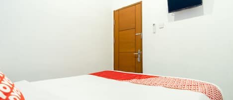 Una habitación de hotel con una cama, una puerta de madera y un televisor pequeño en la pared.