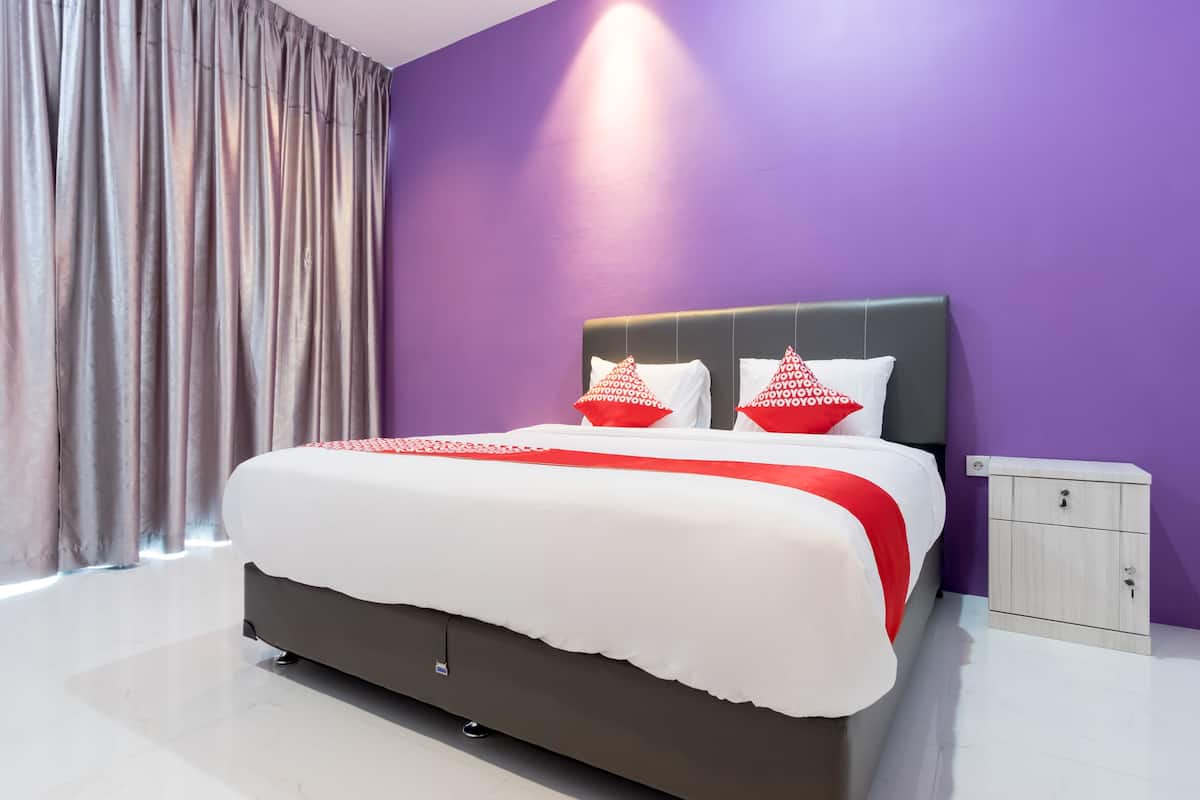 A modern hotel room with a large bed, a nightstand, and a purple wall.