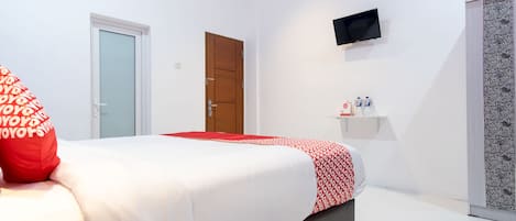 A bedroom with a bed, a television mounted on the wall, a door, and a small shelf with items.