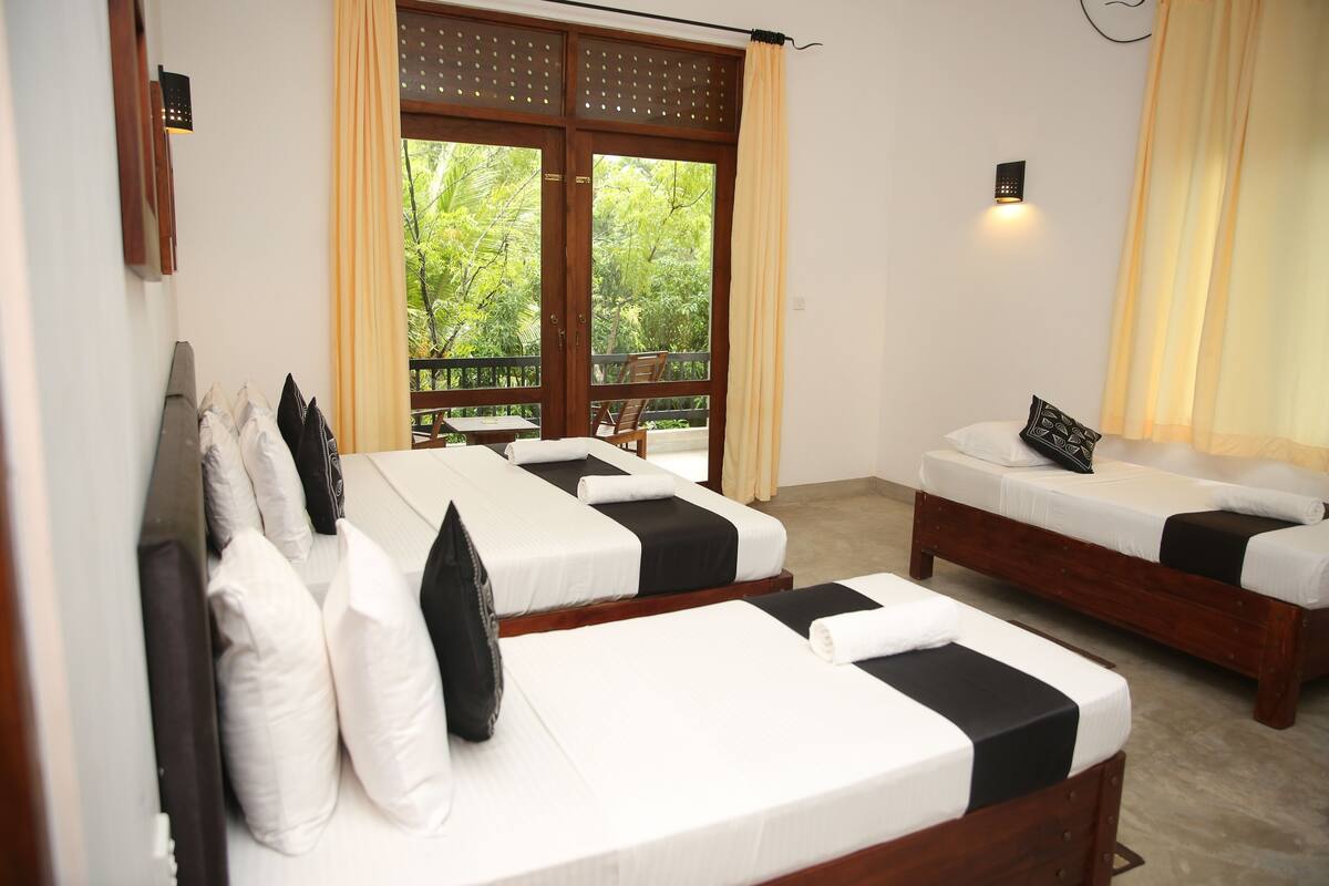 A room with two beds, a balcony, and a view of greenery.