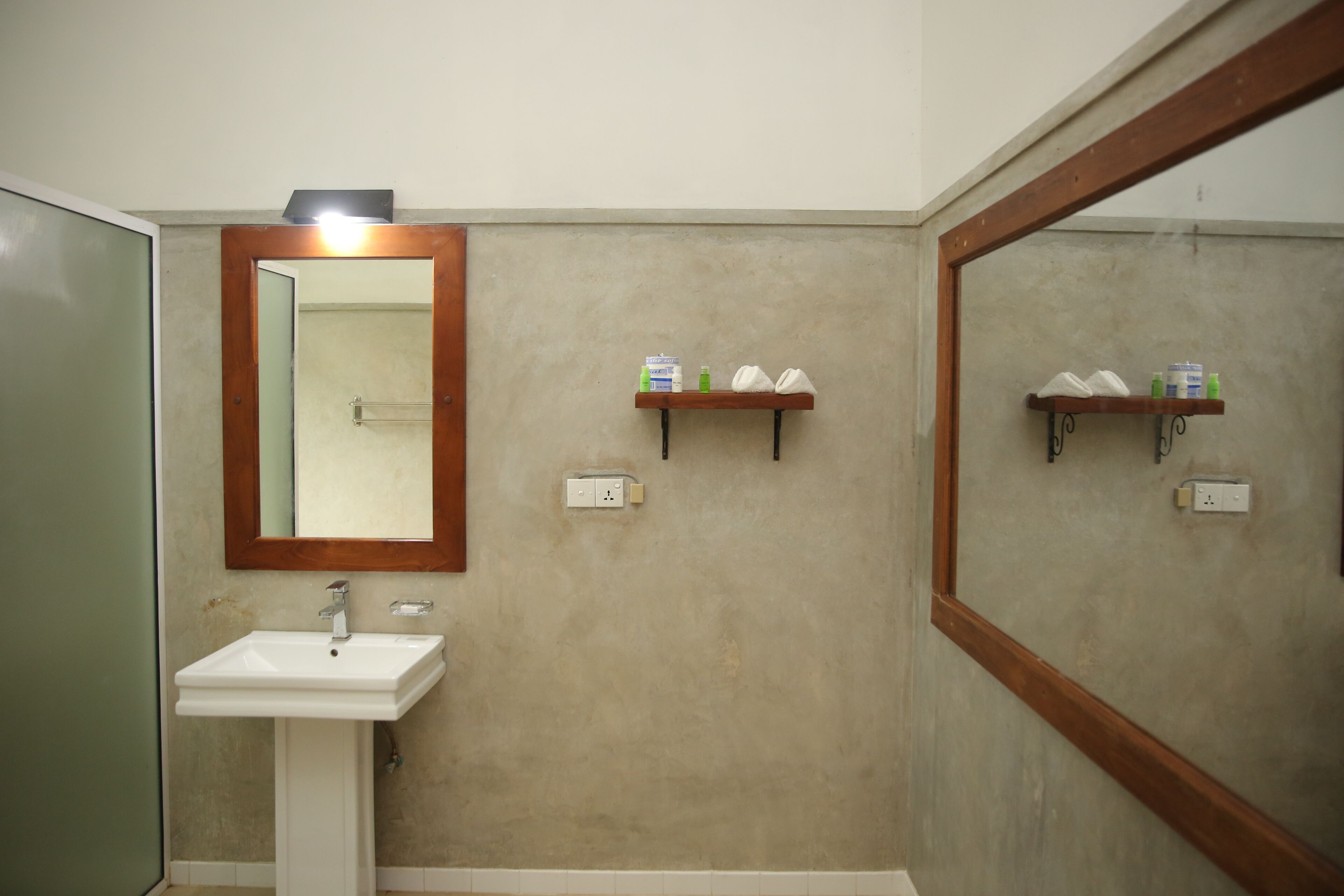 A bathroom with a white sink, a mirror with a wooden frame, and two shelves with toiletries.
