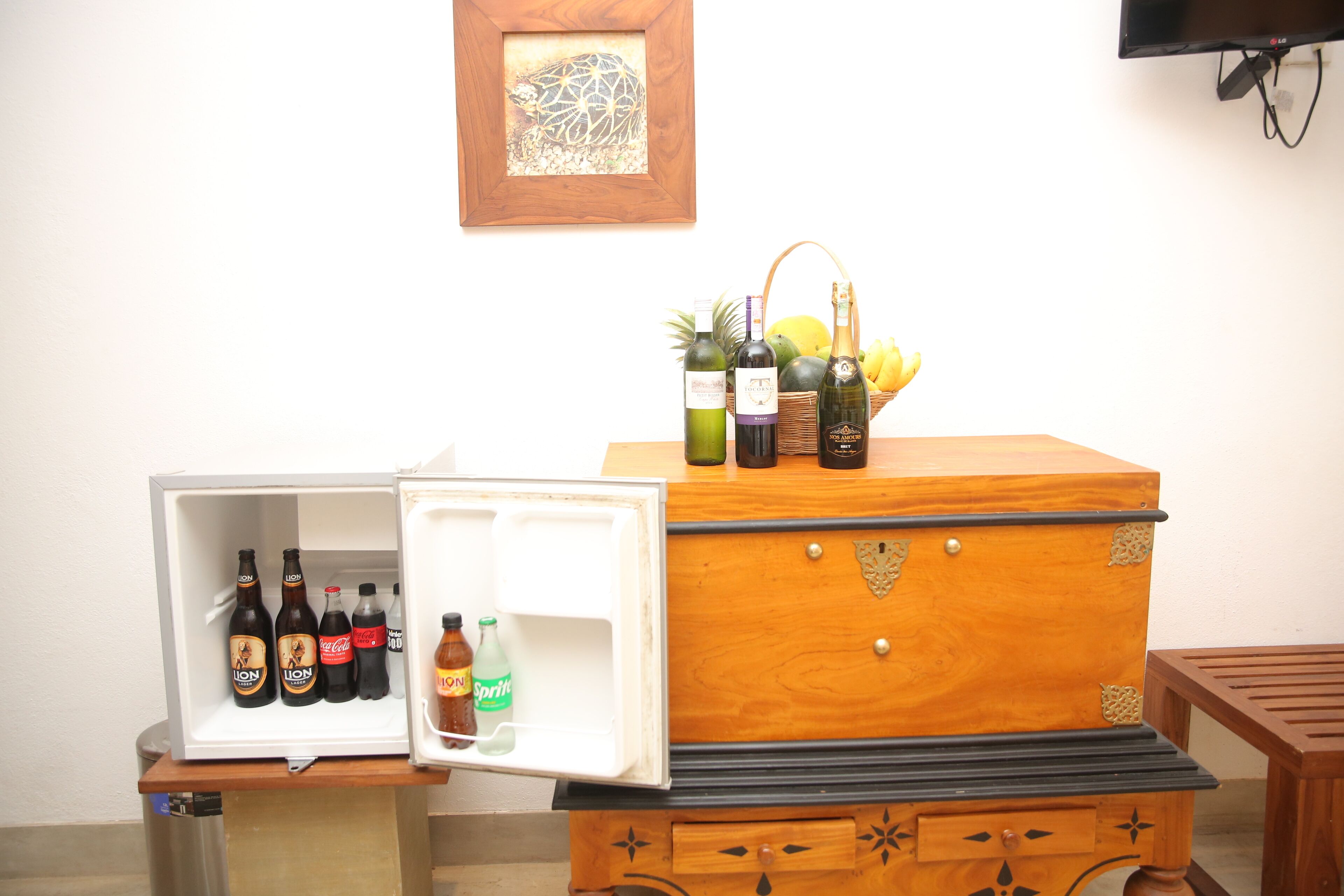 Un refrigerador con bebidas y un cofre de madera con botellas encima.