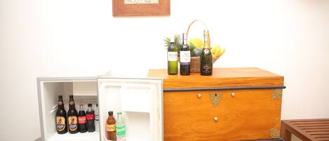 Un refrigerador con bebidas y un cofre de madera con botellas encima.