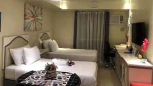 A hotel room with two beds, a desk with a TV, a small table with a flower vase, and a colorful abstract painting on the wall. - I.T PARK CEBU TWIN BED DELUXE FREE FAST WIFI & POOL (Cebu City)