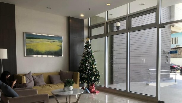 A modern lobby with a large window, a Christmas tree, and a sofa with a person using a mobile device. - I.T PARK CEBU TWIN BED DELUXE FREE FAST WIFI & POOL (Cebu City)