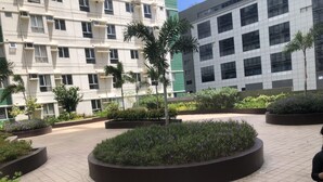 A courtyard with circular planters, a palm tree, and a building with multiple windows. - I.T PARK CEBU TWIN BED DELUXE FREE FAST WIFI & POOL (Cebu City)