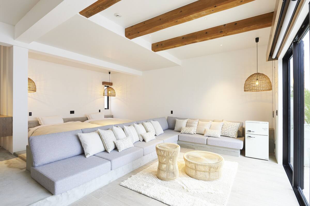 Een moderne woonkamer met een hoekbank, een kleine witte koelkast en een groot raam.