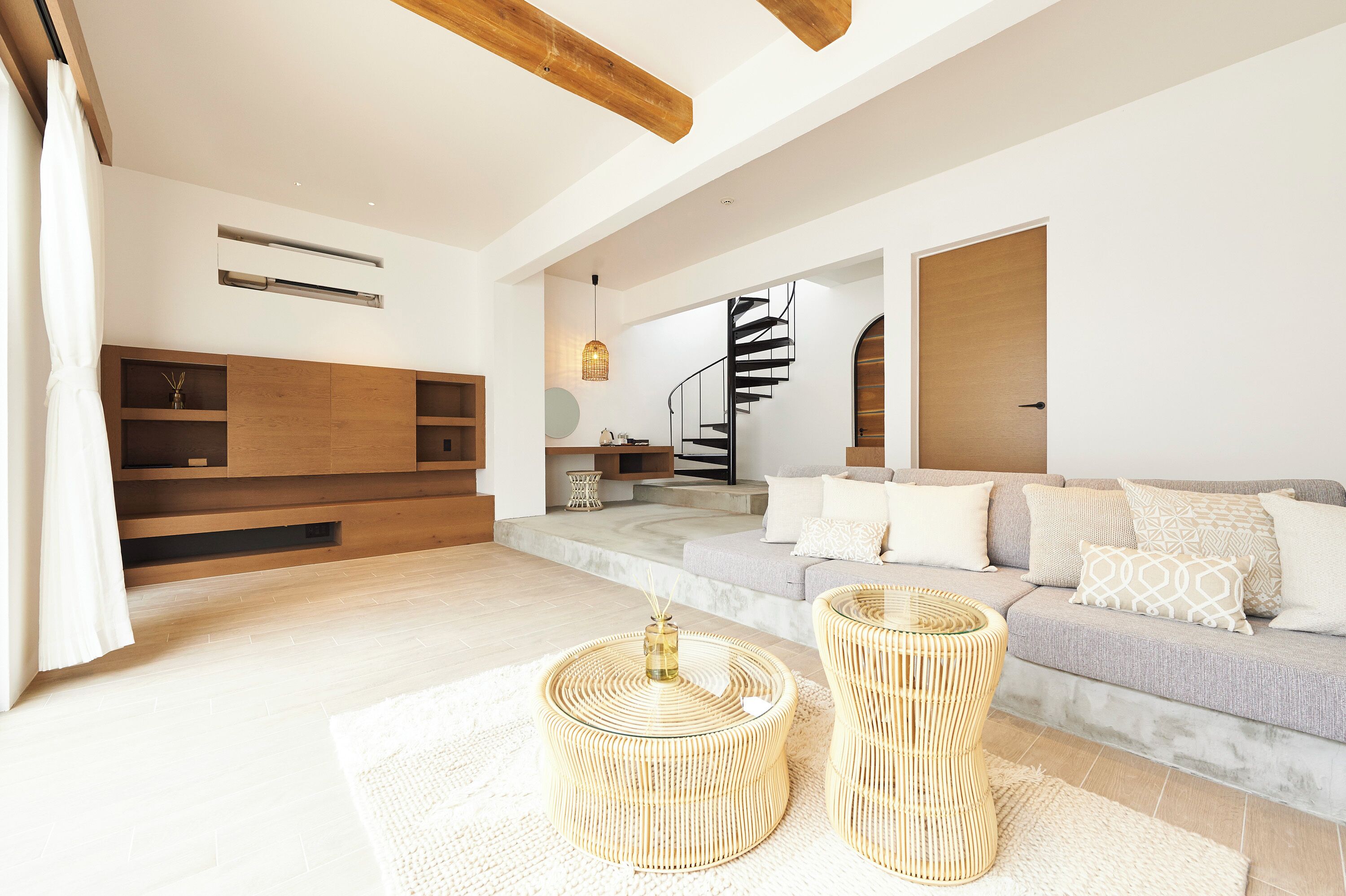 Uma sala de estar moderna com escada, vigas de madeira, um sofá e duas mesinhas de centro redondas de vime.