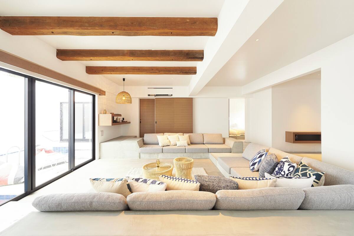 Een moderne woonkamer met een ruime modulaire bank, een eethoek en een uitzicht door grote ramen.
