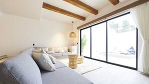 Uma sala de estar moderna com um sofá cinzento, mesinhas de cabeceira de vime e uma grande porta de vidro deslizante que dá para uma área externa.