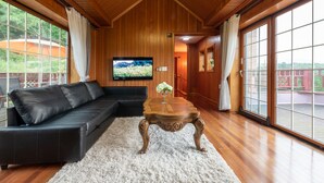 A wooden-paneled room with a black leather sofa, a wooden coffee table, and a large window with curtains. - The Hue Largo Bundang (Yongin)