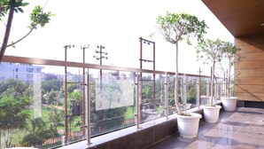 A balcony with potted plants and a view of a cityscape. - Kumar Residency (Noida)