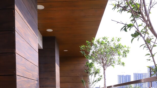 A corridor with wooden paneling, potted plants, and a glass railing overlooking a cityscape. - Kumar Residency (Noida)
