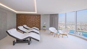 Ein moderner Spa-Raum mit Massagetischen, einem kleinen Tisch mit Blumenvase und Blick auf eine Marina durch große Fenster.