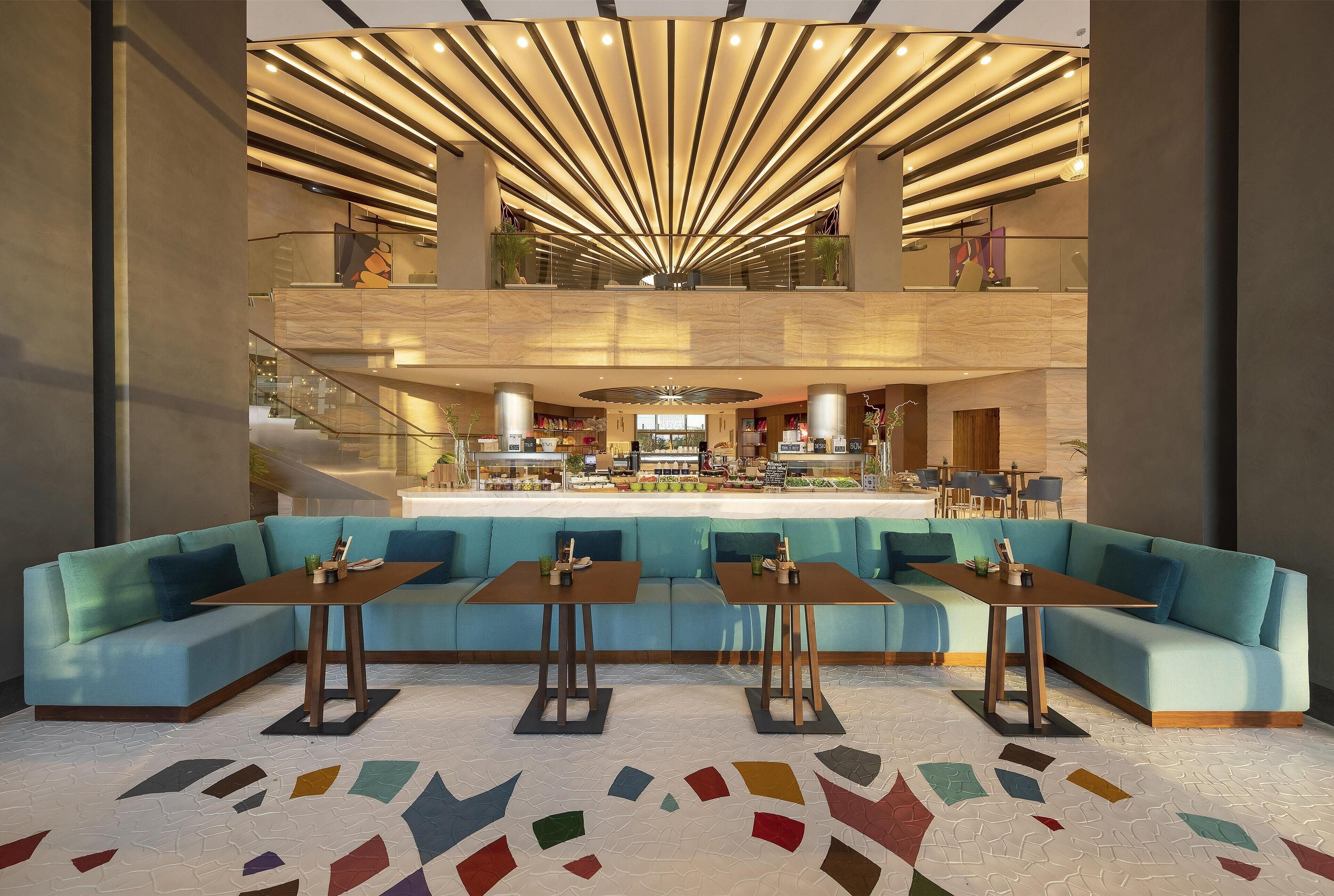 A modern lobby with a central seating area, a staircase, and a reception desk.